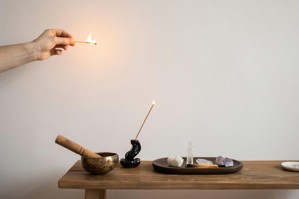A hand lighting incense near a display of crystals and a mortar on a wooden table.